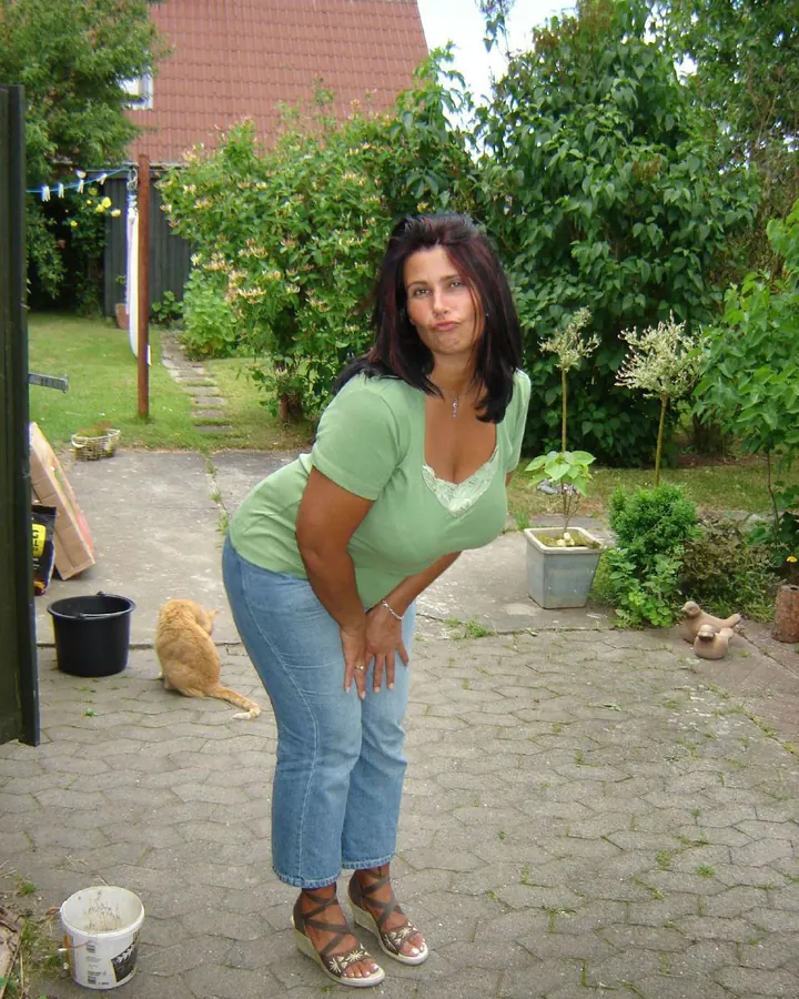 Femme latine d'une cinquantaine d'années, debout dans un jardin, portant un t-shirt vert et un jean, les mains sur les hanches.