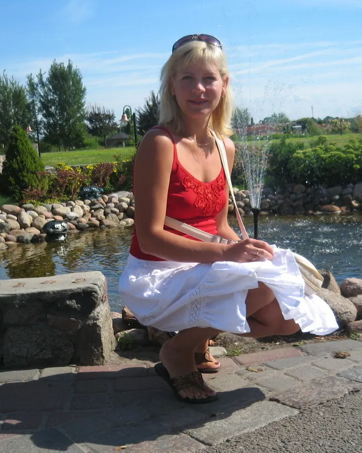Femme blonde en débardeur rouge et jupe blanche, accroupie près d'un bassin