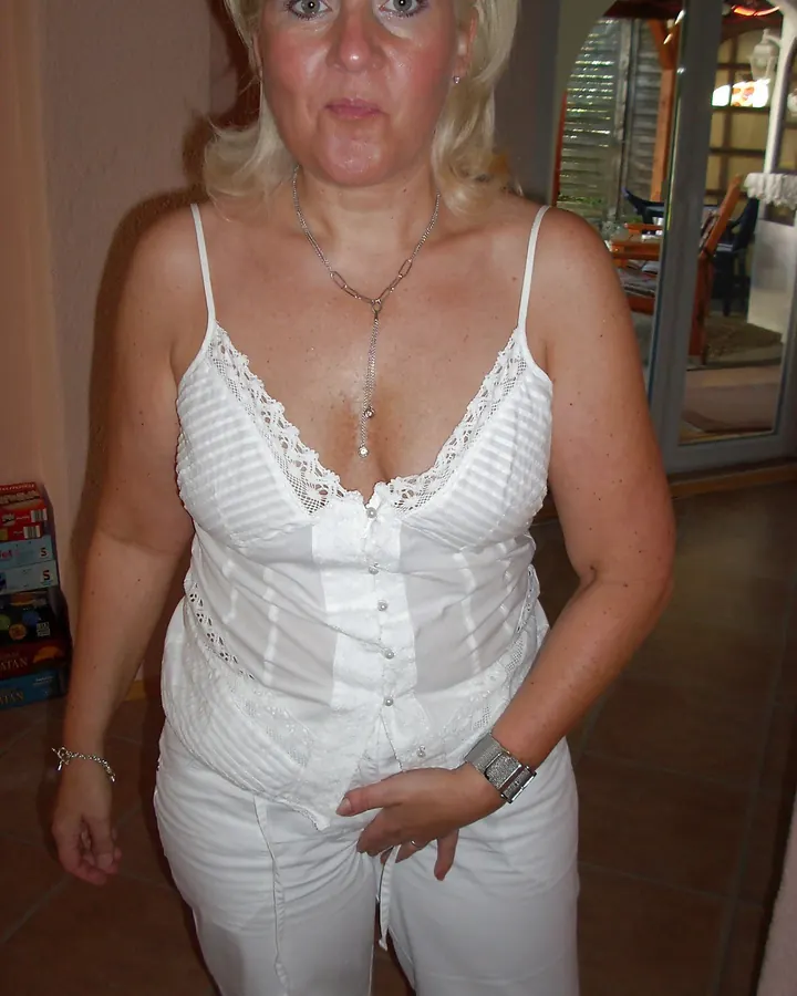 Femme blonde en tenue blanche, regard direct, posture neutre dans un intérieur.