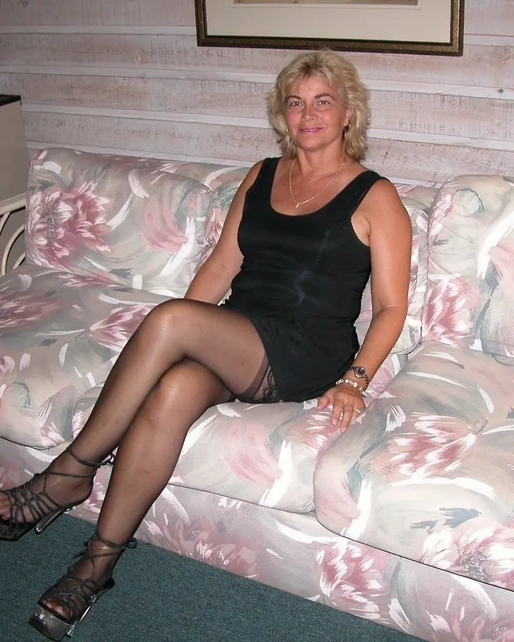 Femme souriante portant une robe noire, bijoux, cheveux blonds courts, en soirée.