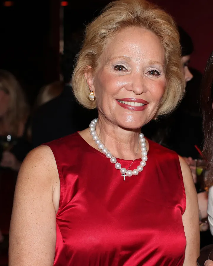 Femme souriante portant une robe rouge, collier de perles, cheveux blonds courts, en soirée.