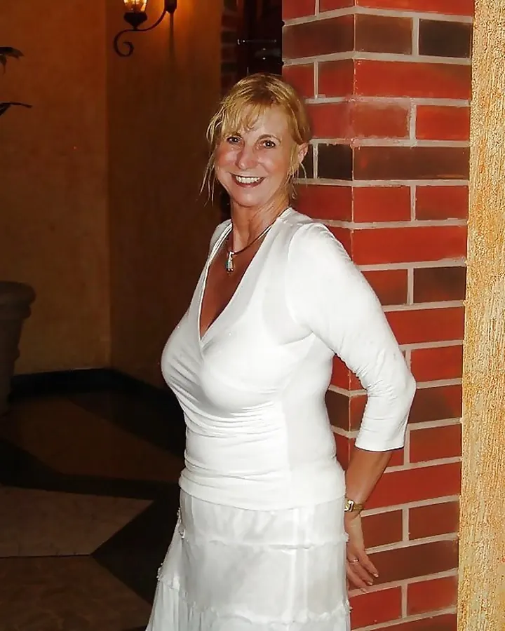 Femme aux cheveux roux en haut noir, posant près d’un lit