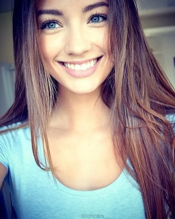 Femme aux cheveux bruns en haut bleu clair, souriant, avec un fond intérieur flou