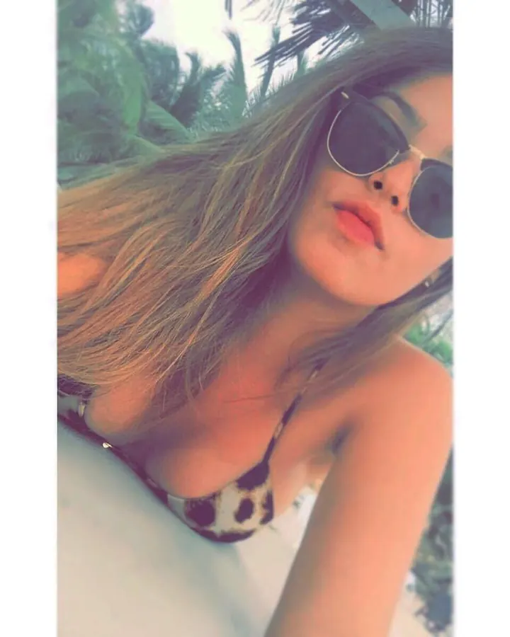 Femme aux cheveux blonds portant un maillot de bain léopard et des lunettes de soleil, en extérieur avec des palmiers.