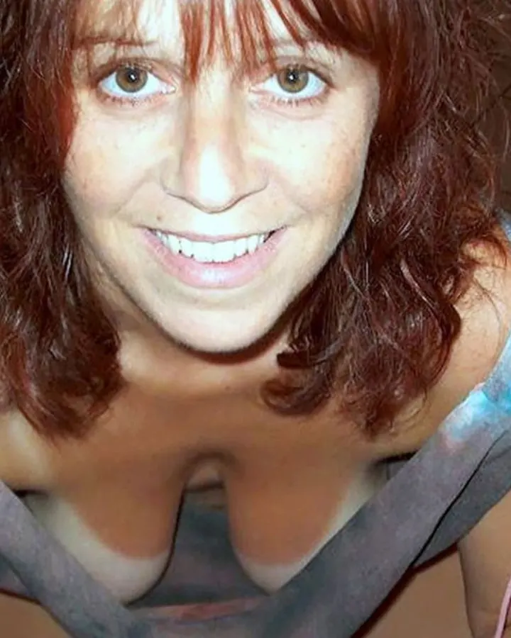 Femme aux cheveux roux, portant un haut noir et un short noir, assise sur un canapé, enchaussée de talons noirs brillants.