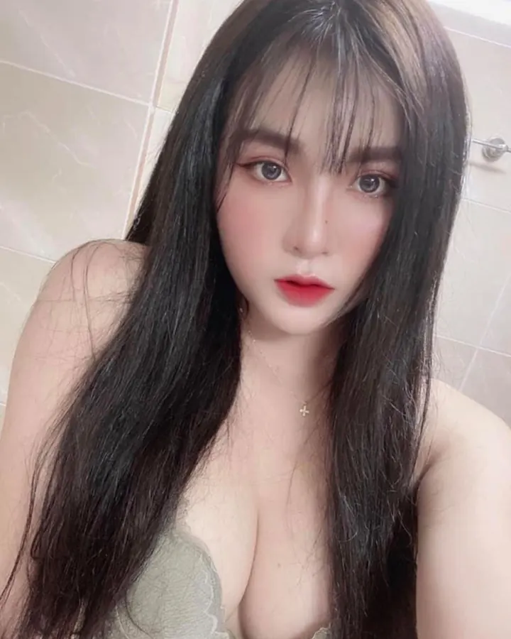 Jeune femme aux cheveux châtains, en haut rose, prenant un selfie dans une salle de bain.