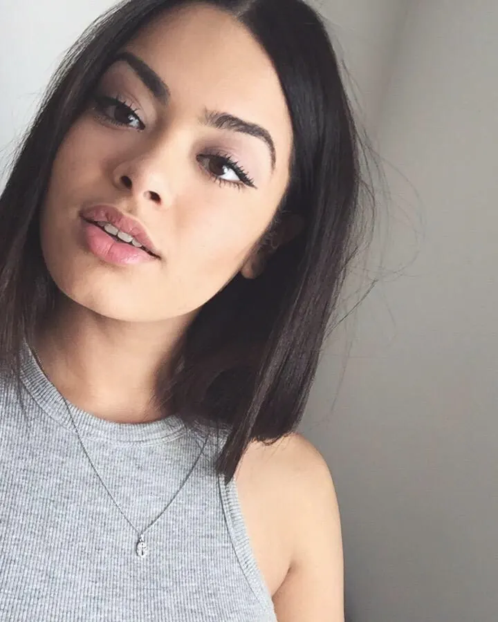 Femme souriante, regardant l'appareil, portant un haut gris sans manches, avec un collier fin.