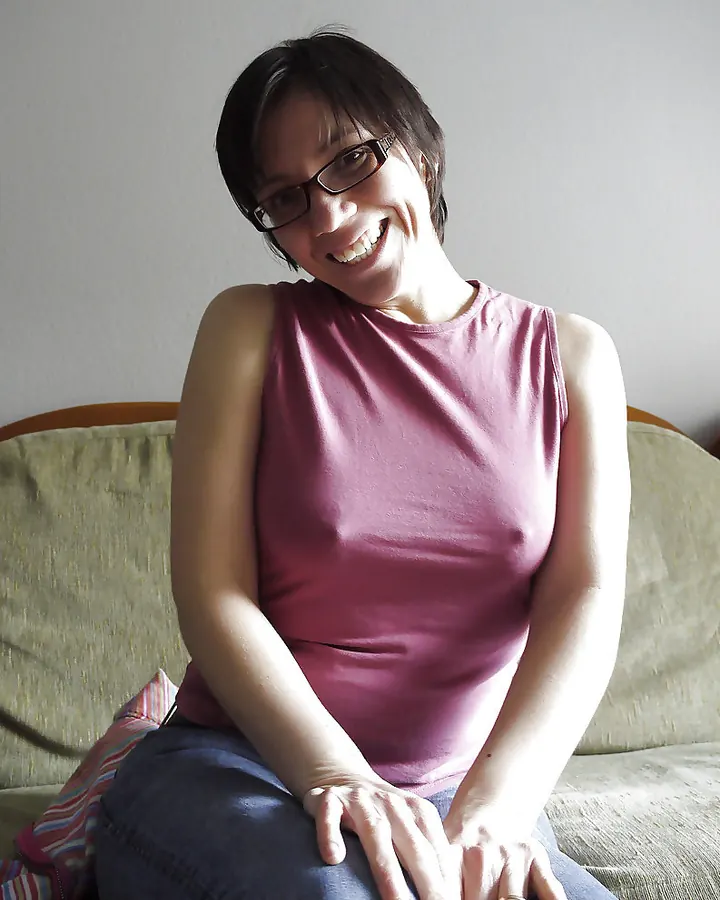 Femme aux cheveux noirs mi-longs, en haut noir transparent, posant dans une chambre.
