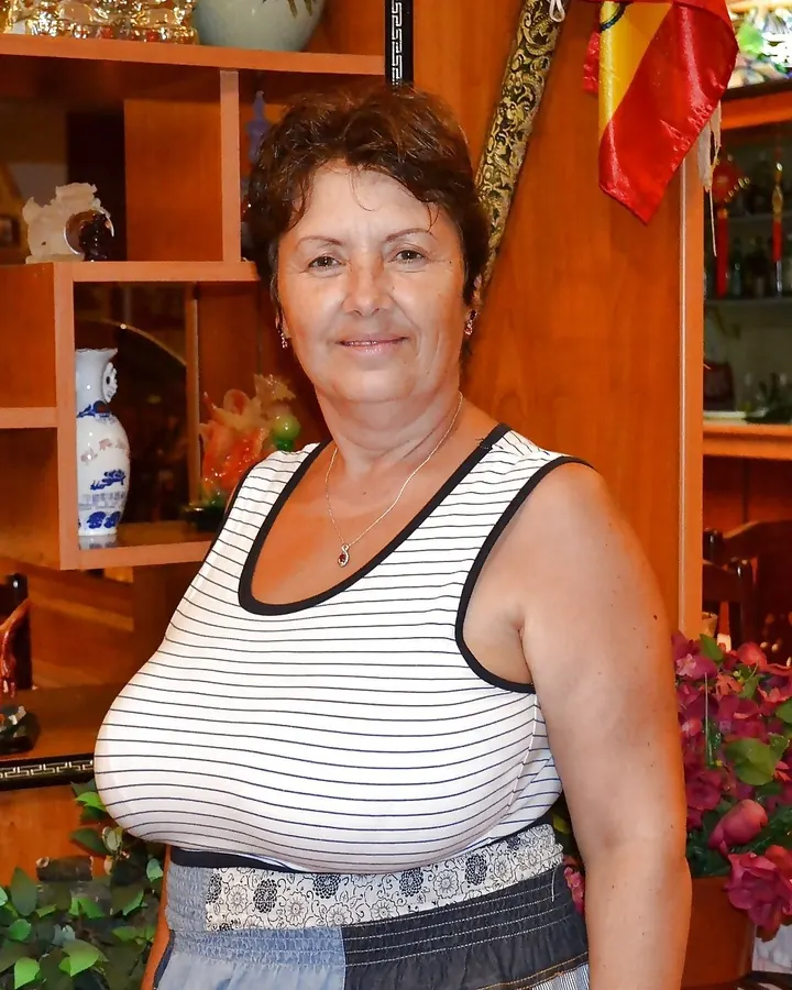 Femme aux cheveux bruns mi-longs, en haut noir transparent, posant dans une chambre.