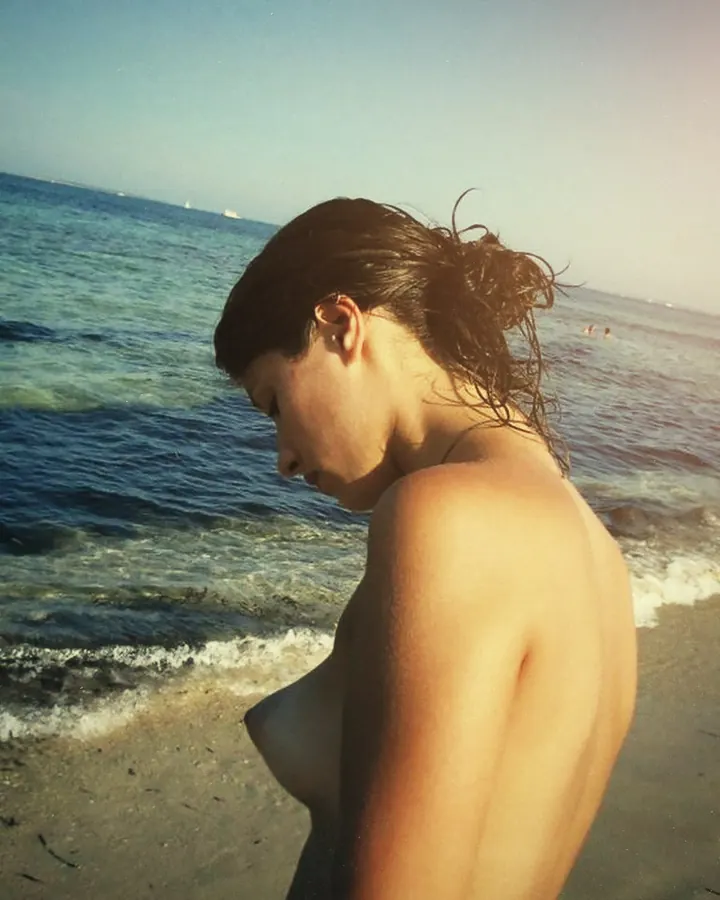 Femme nue sur plage, profil, regard vers le bas, cheveux mouillés