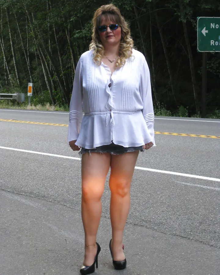 Femme en chemise blanche et mini-jupe noire, debout sur route avec lunettes de soleil