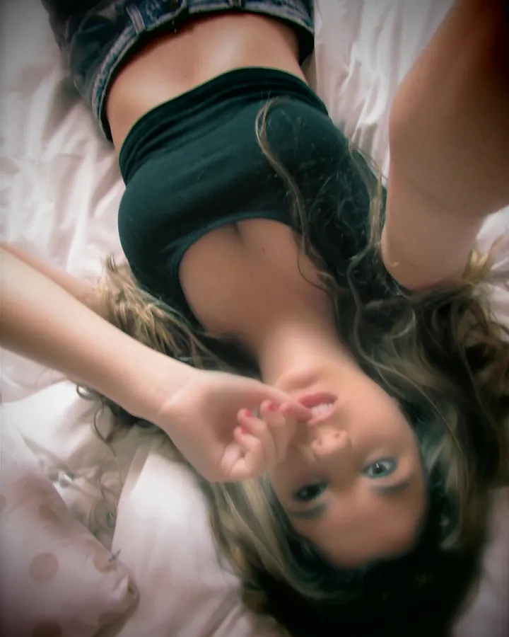 Jeune femme allongée en short et crop top noir, selfie depuis le lit