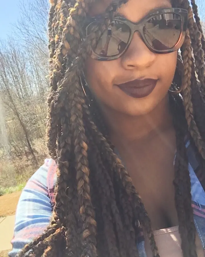 Femme aux cheveux tressés, portant des lunettes de soleil, en gros plan.