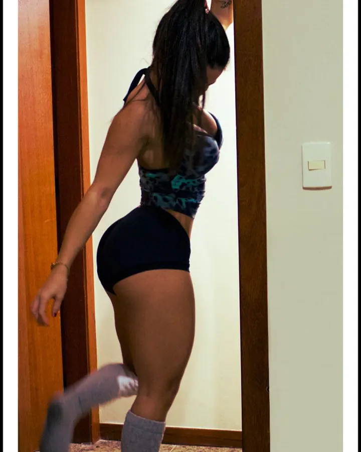 Femme latino aux cheveux châtains, portant un haut gris et une culotte blanche, prenant un selfie devant un miroir.